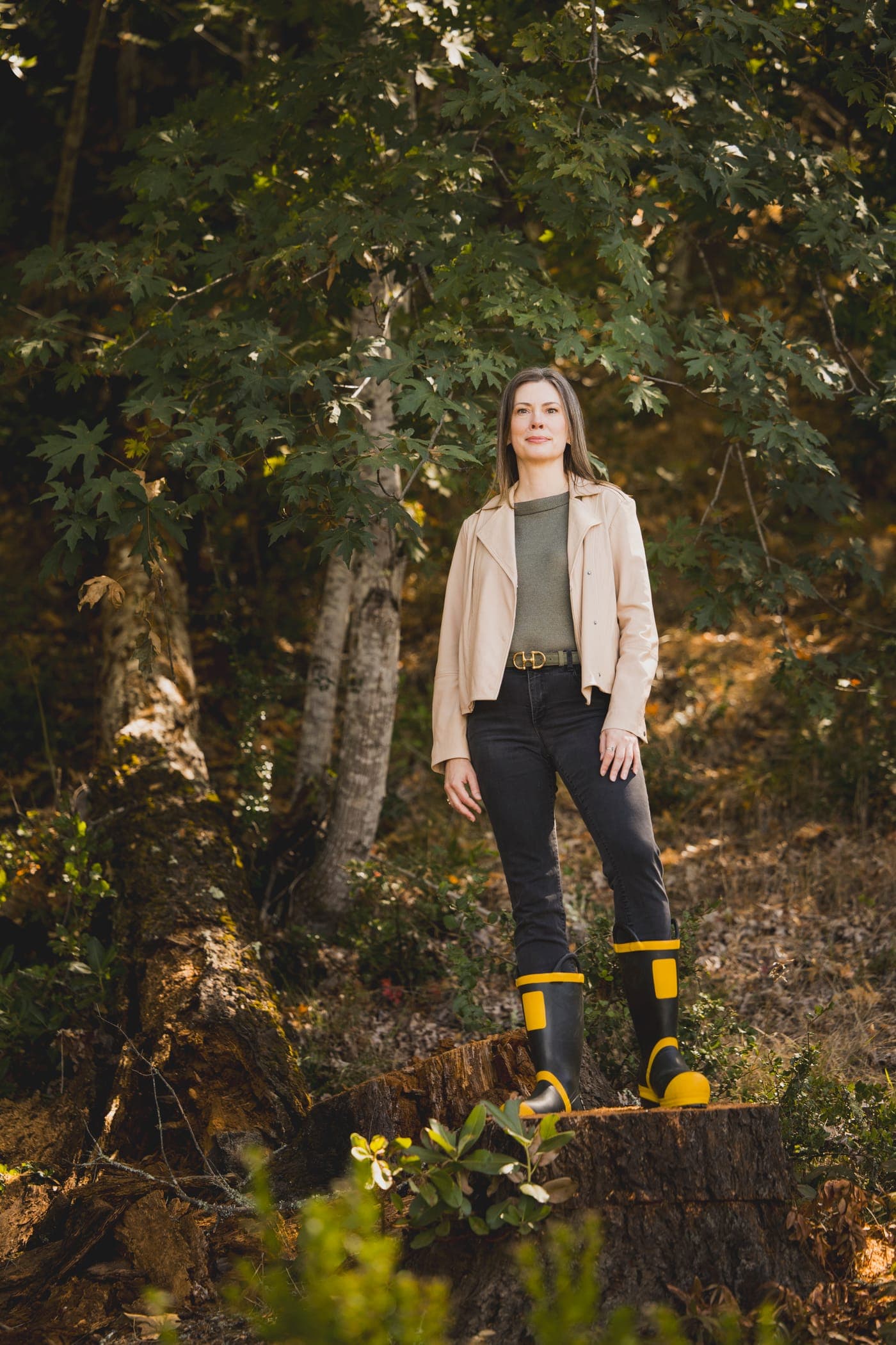 Kathleen Defever standing on a tree stump in the woods, wearing her fire boots