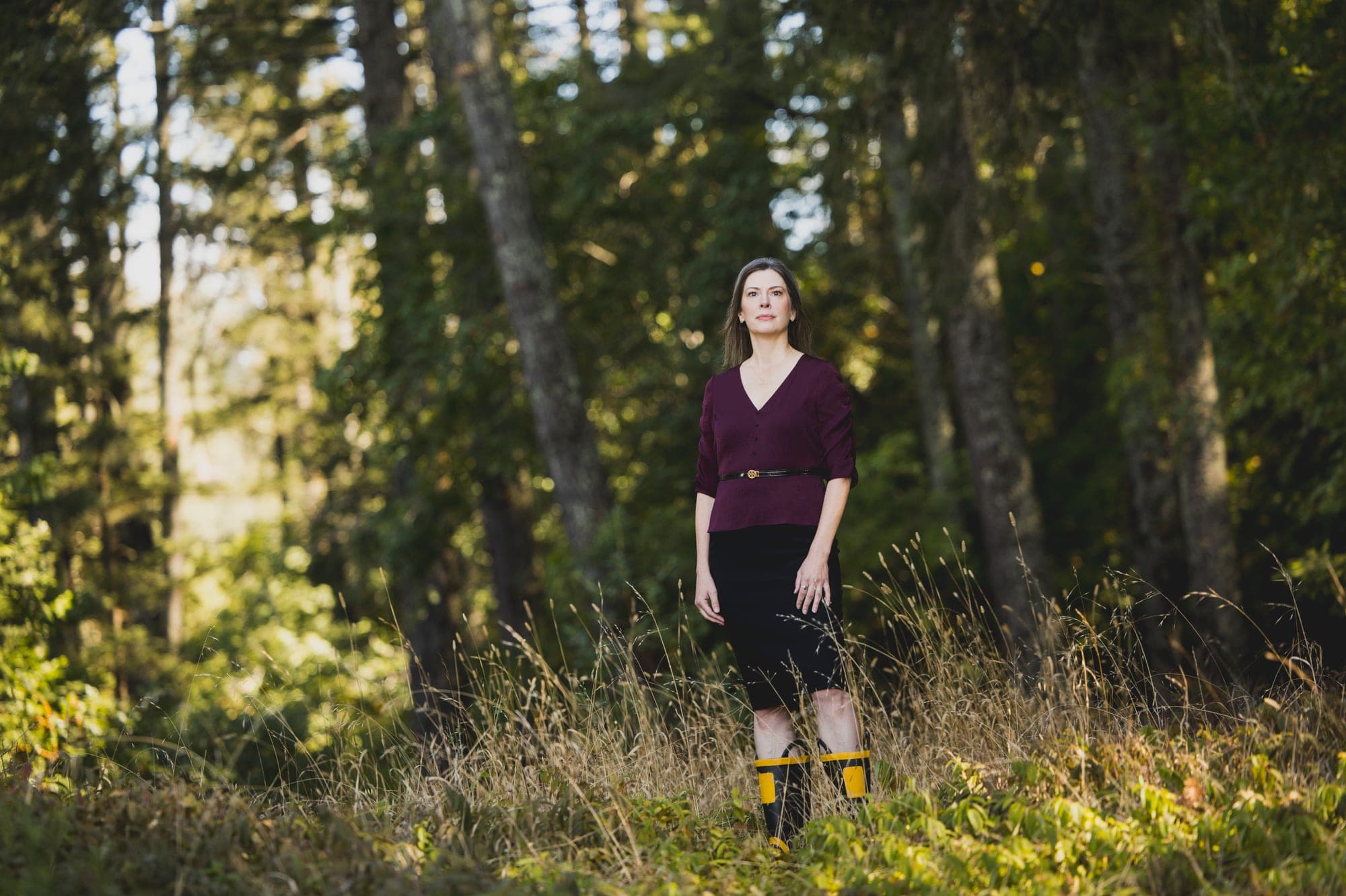Kathleen Defever standing in tall grass among trees, wearing her yellow-and-black fire boots